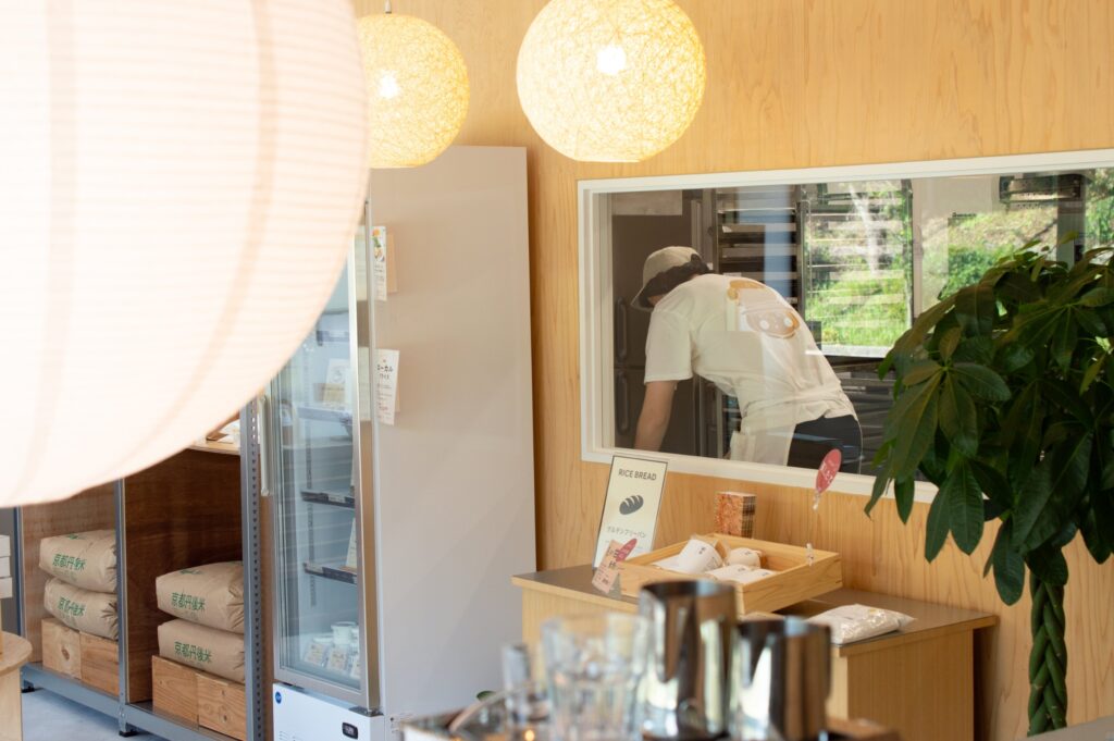 木の壁と大きな照明の向こうに、ガラス越しで働くスタッフが見える、ファームベイク京都の店内